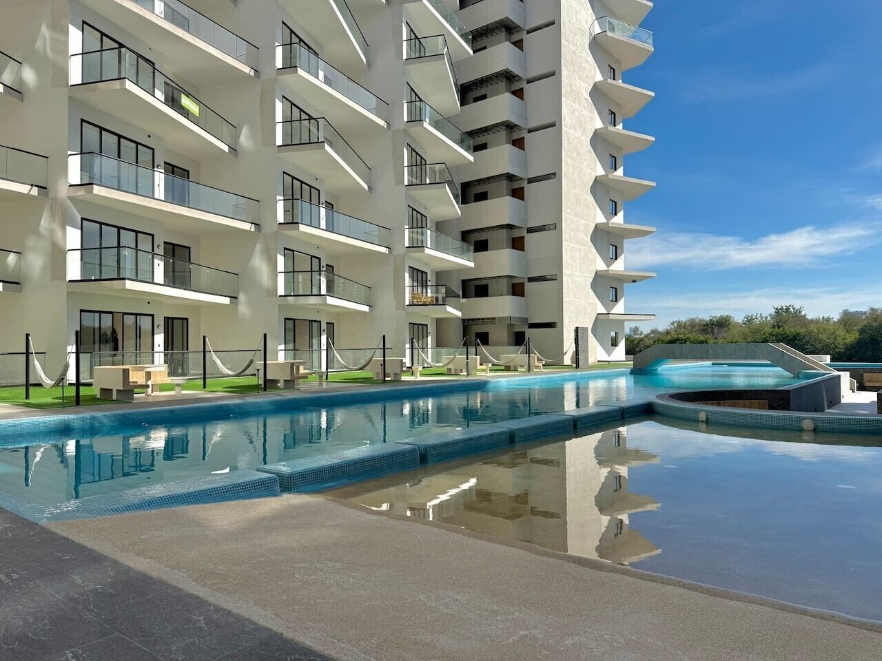 A modern hotel with a pool area, multiple balconies, and a clear sky.