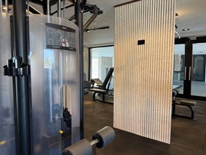 Ein Fitnessraum mit Trainingsgeräten, einer Wand mit vertikalen Linien und einer Sitzbank.