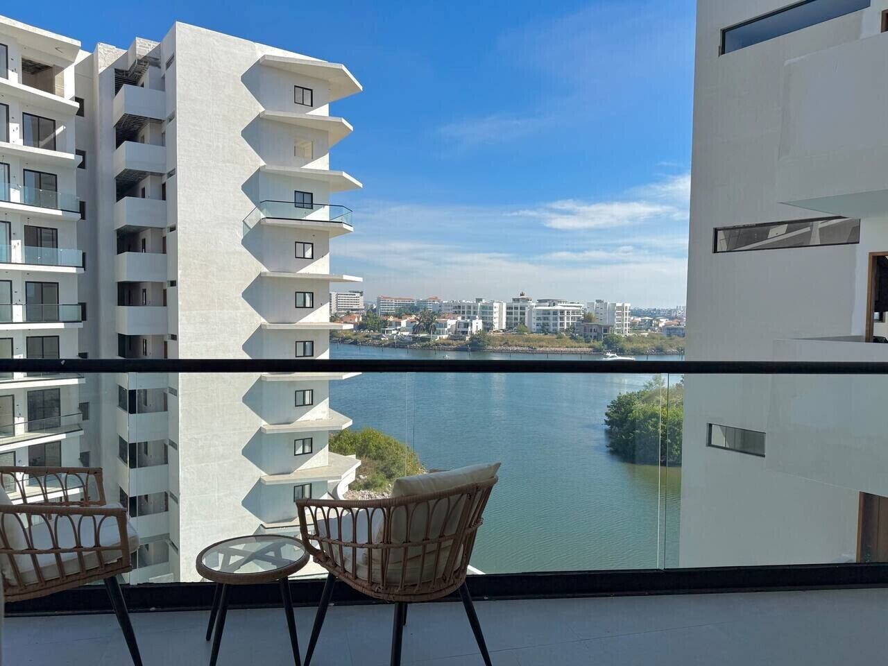 A balcony with a view of a river and cityscape, furnished with wicker chairs and a small table.