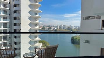 A balcony with a view of a river and cityscape, furnished with wicker chairs and a small table.