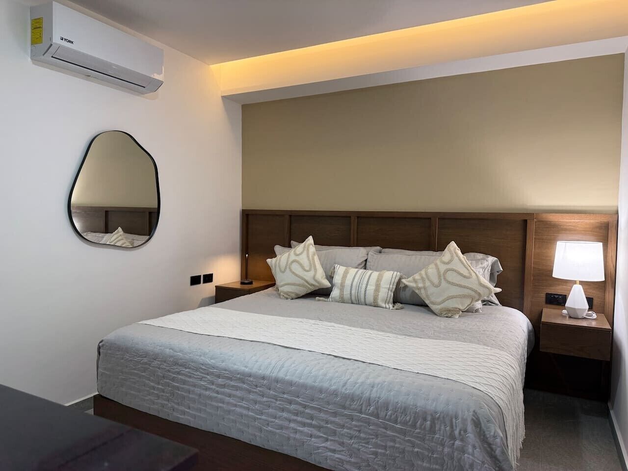 A hotel room with a bed, a bedside lamp, a wall-mounted air conditioner, and a mirror.