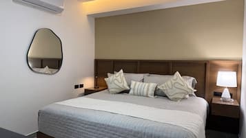 A hotel room with a bed, a bedside lamp, a wall-mounted air conditioner, and a mirror.