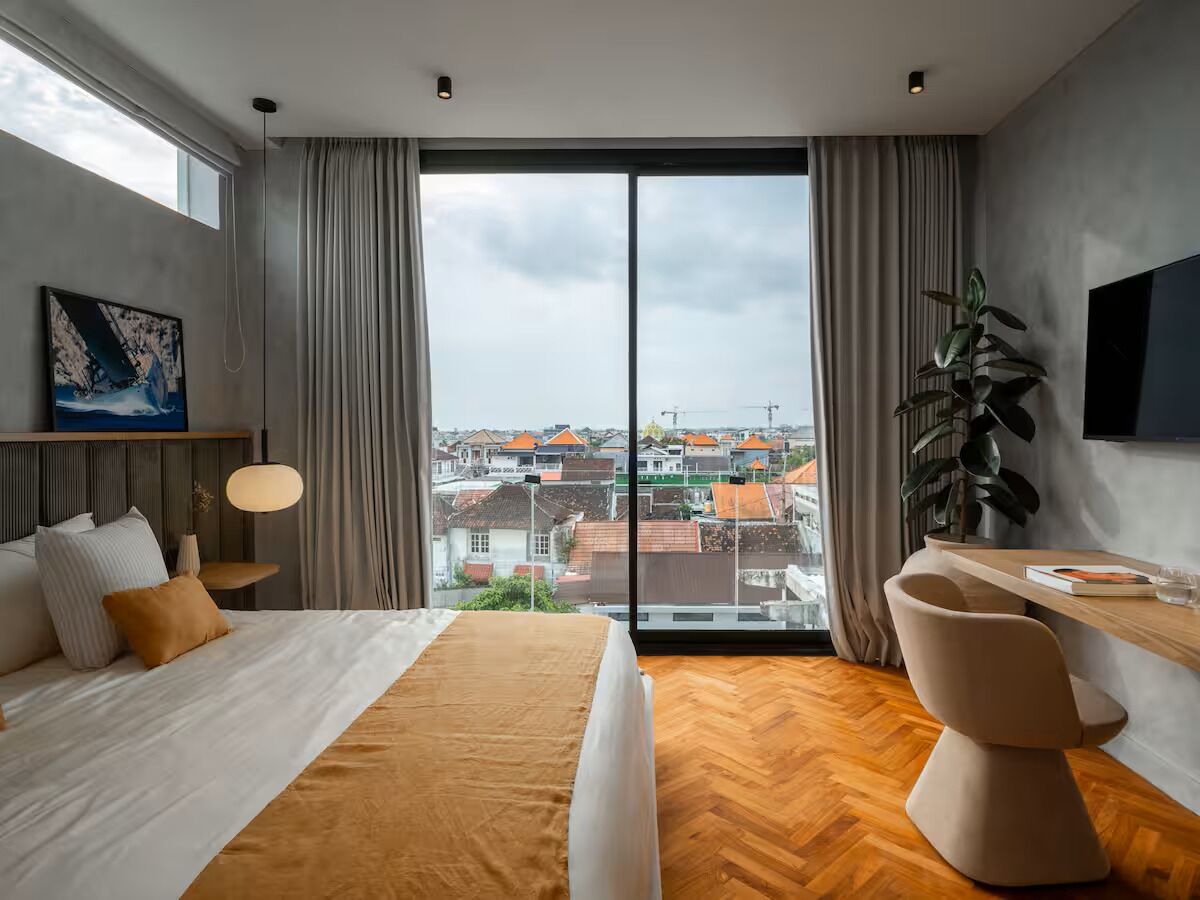 A modern hotel room with a large window, a bed, a desk, and a chair.