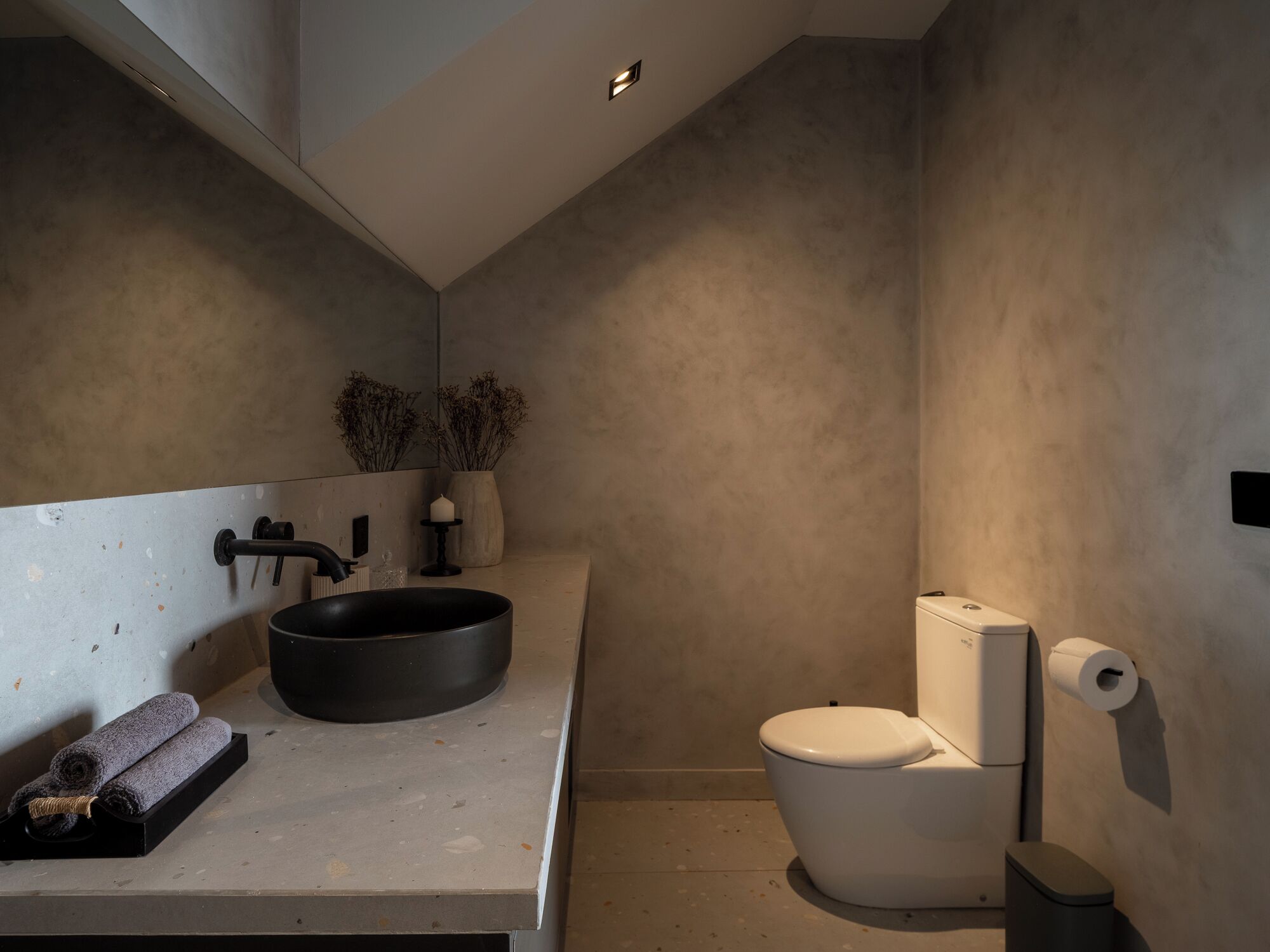 A modern bathroom with a large black sink, a toilet, and a small mirror.