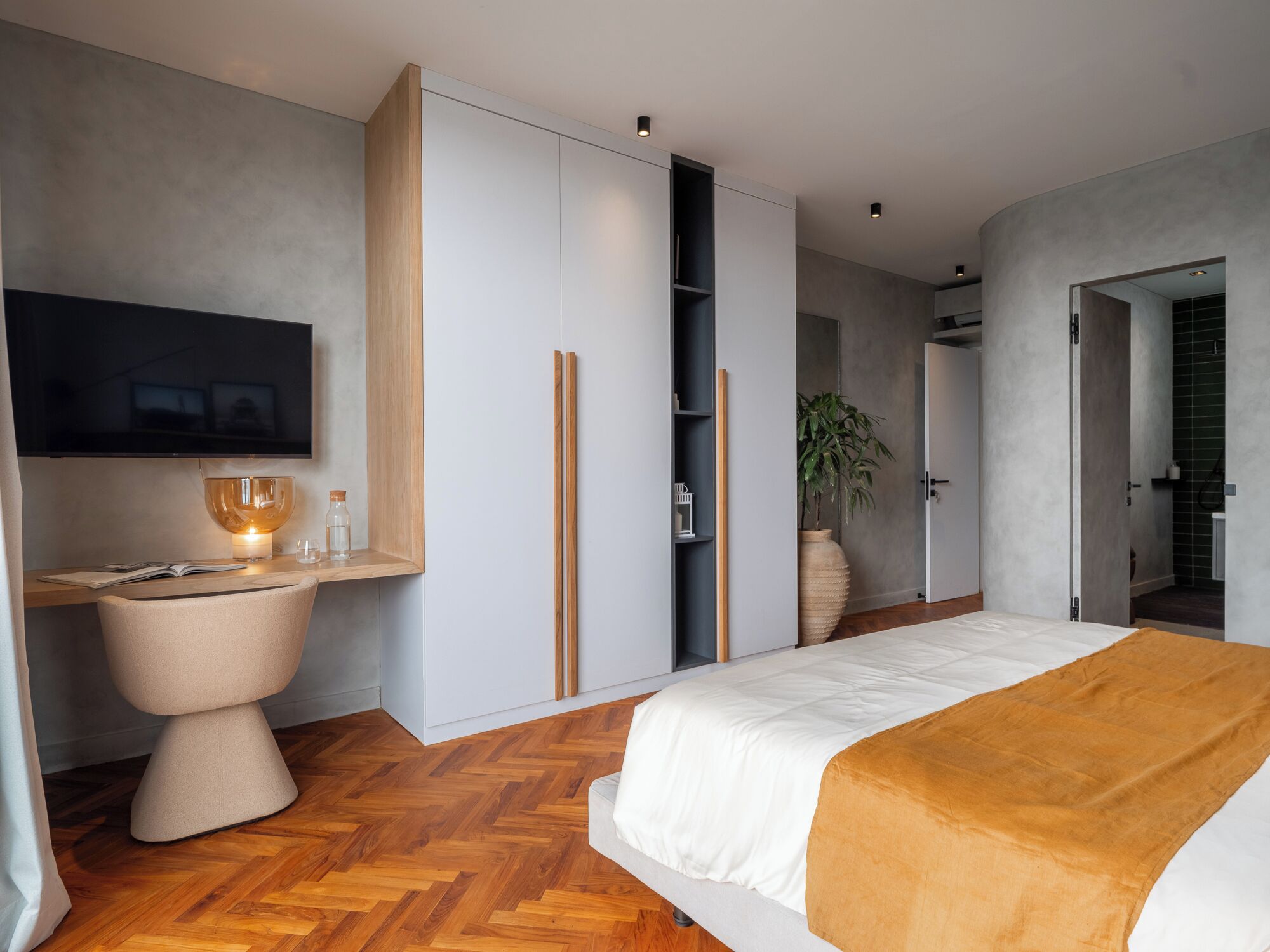 A modern bedroom with a large bed, a television, a desk with a lamp, and built-in wardrobes.