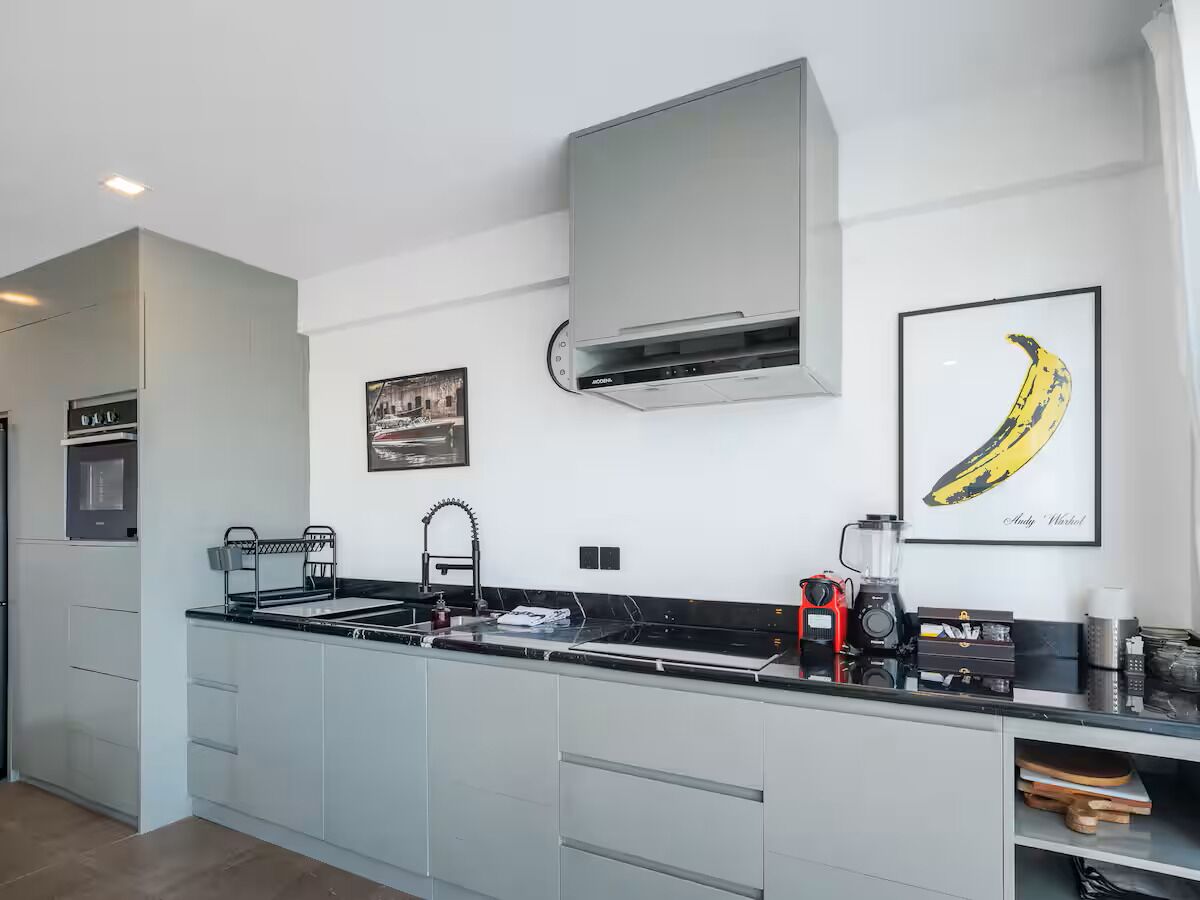 A modern kitchen with a built-in oven, a gas stove, a sink, and a microwave. There is a framed picture on the wall and a banana artwork.