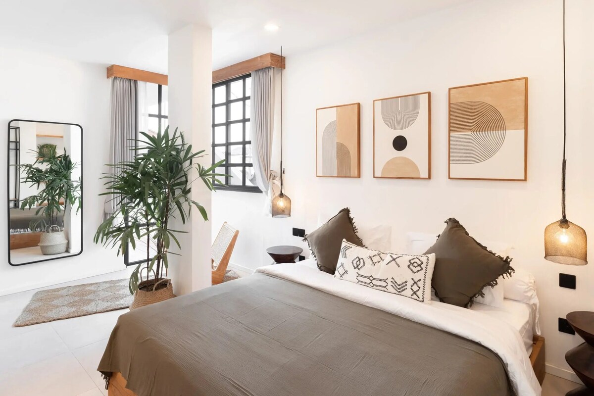 Ein modernes Schlafzimmer mit einem großen Bett, einer Topfpflanze und Bildern an den Wänden.