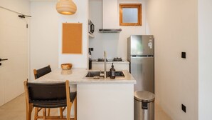 A compact kitchen with a central island, a stainless steel refrigerator, a hanging light fixture, and a small window. - Tribeca Bali (Bali)