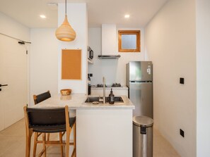 Eine kompakte Küche mit einer zentralen Kochinsel, einem Edelstahlkühlschrank, einer Pendelleuchte und einem kleinen Fenster.