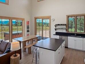 Eine moderne Küche mit Kochinsel, weißen Schränken und großen Fenstern mit Blick ins Freie.
