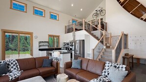 A spacious living area with a brown leather sofa, a coffee table, and a dining area with a kitchen in the background. - LEED Gold Retreat | Hot Tub | Near Tamarack (Donnelly)