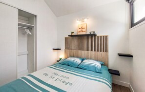 Une chambre à coucher comprenant un lit, des tables de chevet, une commode, une étagère fixée au mur, une lampe de chevet, un tableau décoratif et une armoire avec des vêtements suspendus.
