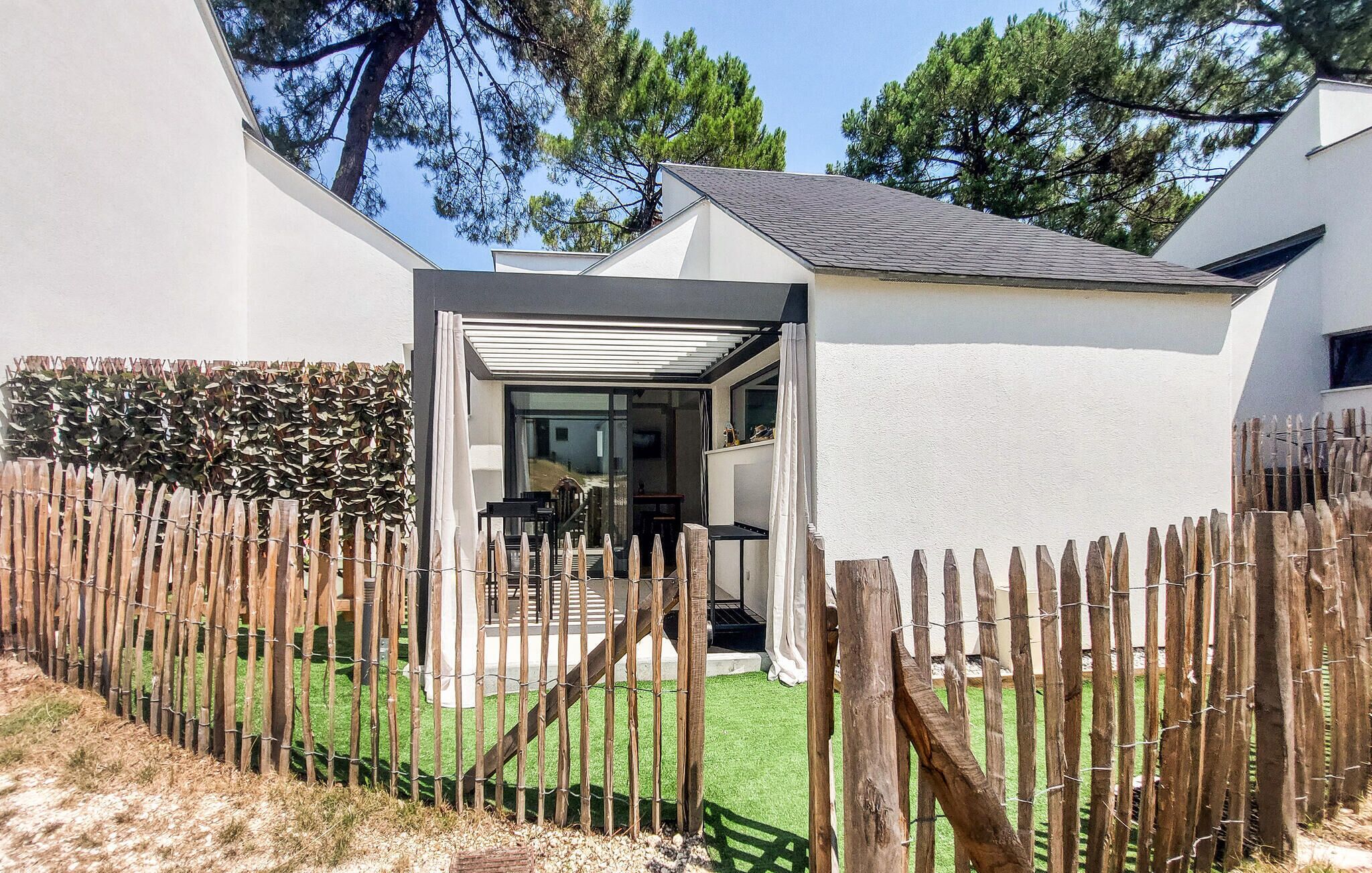 Ein modernes Haus mit überdachter Terrasse, Holzzaun und gepflegtem Rasen.