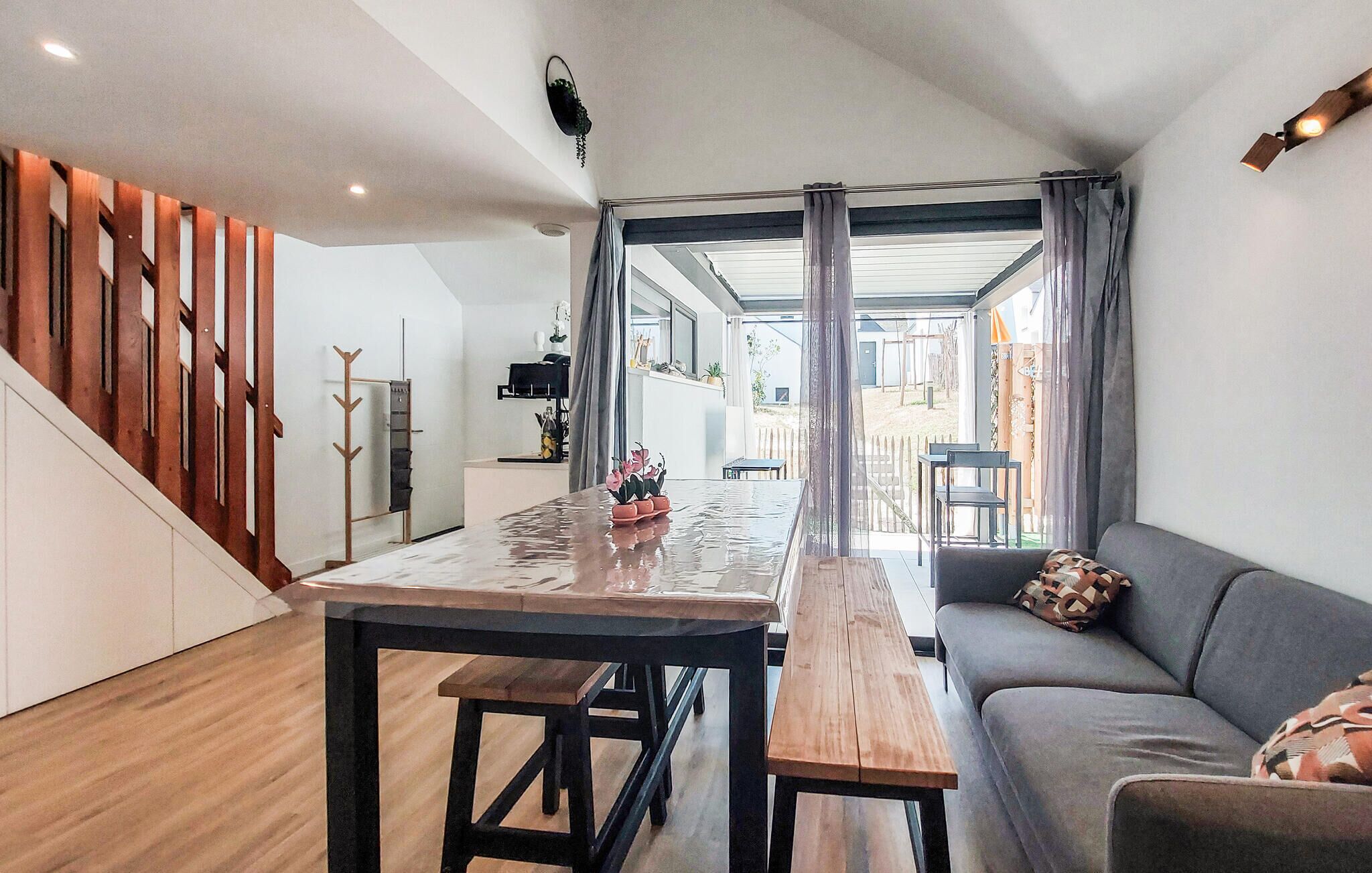Een moderne leefruimte met een houten trap, een eethoek met een tafel en banken, en een bank met een gestreept kussen.
