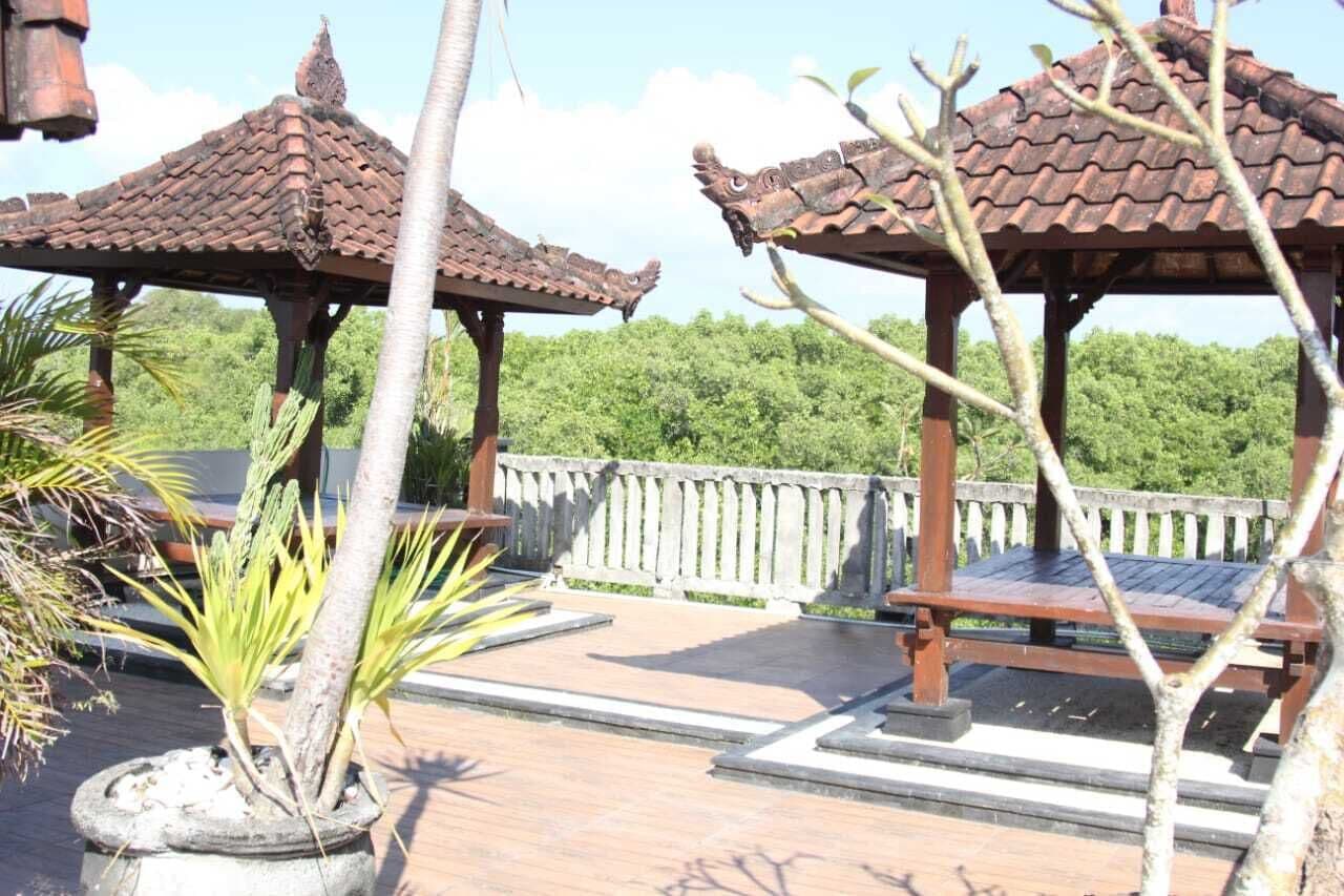 A gazebo with a tiled roof, surrounded by a stone balustrade, set in a landscaped garden with a palm tree and a potted plant.