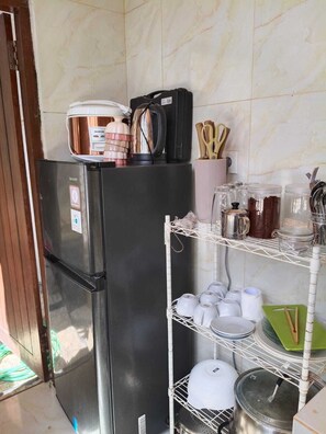 Cuina amb nevera negra, cafetera i diversos utensilis de cuina a les prestatgeries.