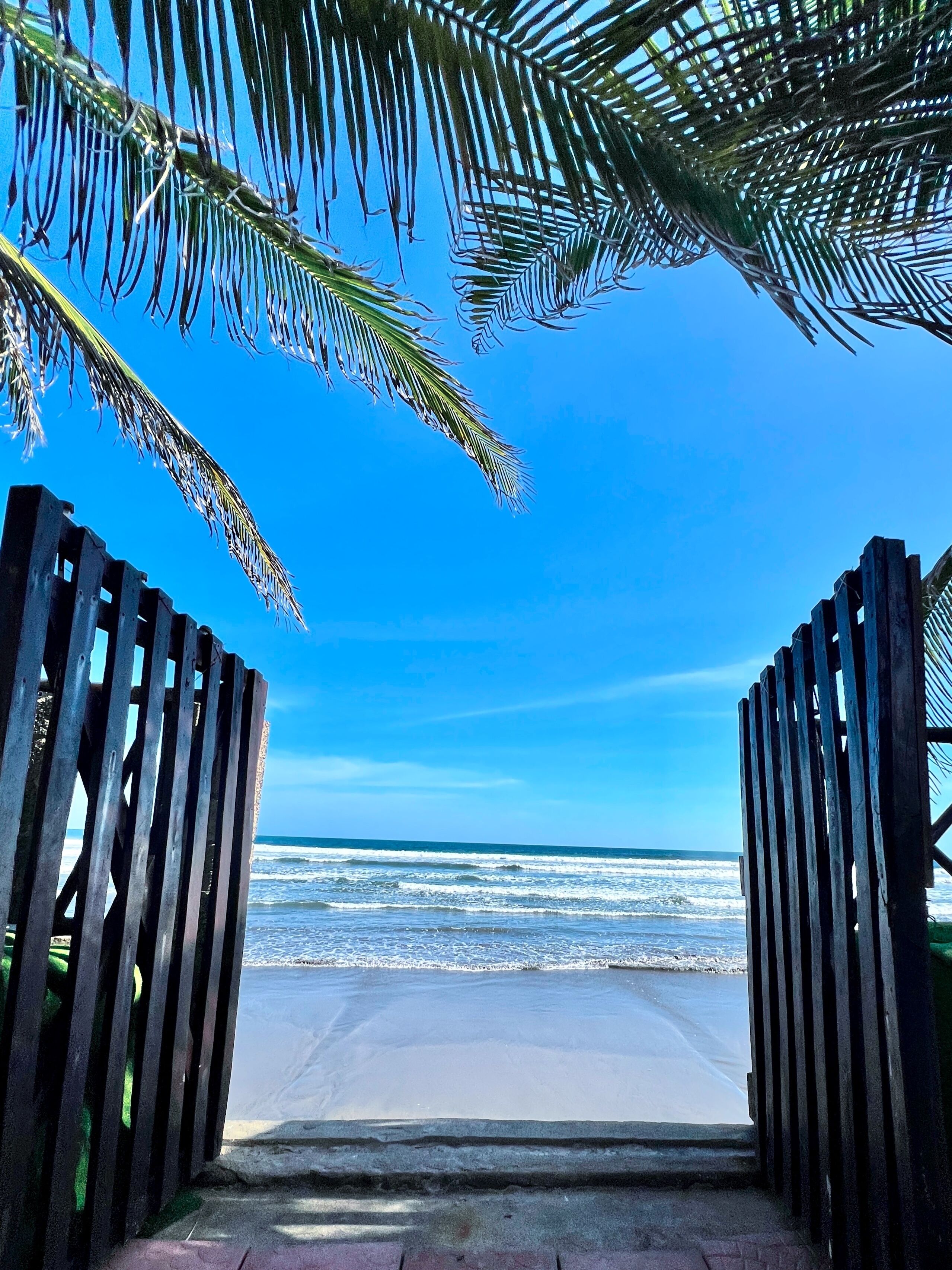 A wooden gate leading to a beach with a clear view of the ocean.