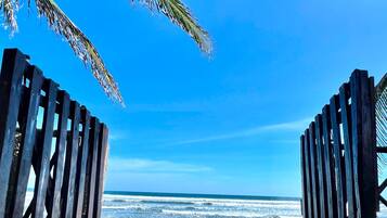 A wooden gate leading to a beach with a clear view of the ocean.