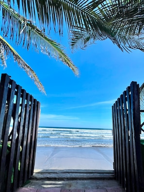 A wooden gate leading to a beach with a clear view of the ocean.