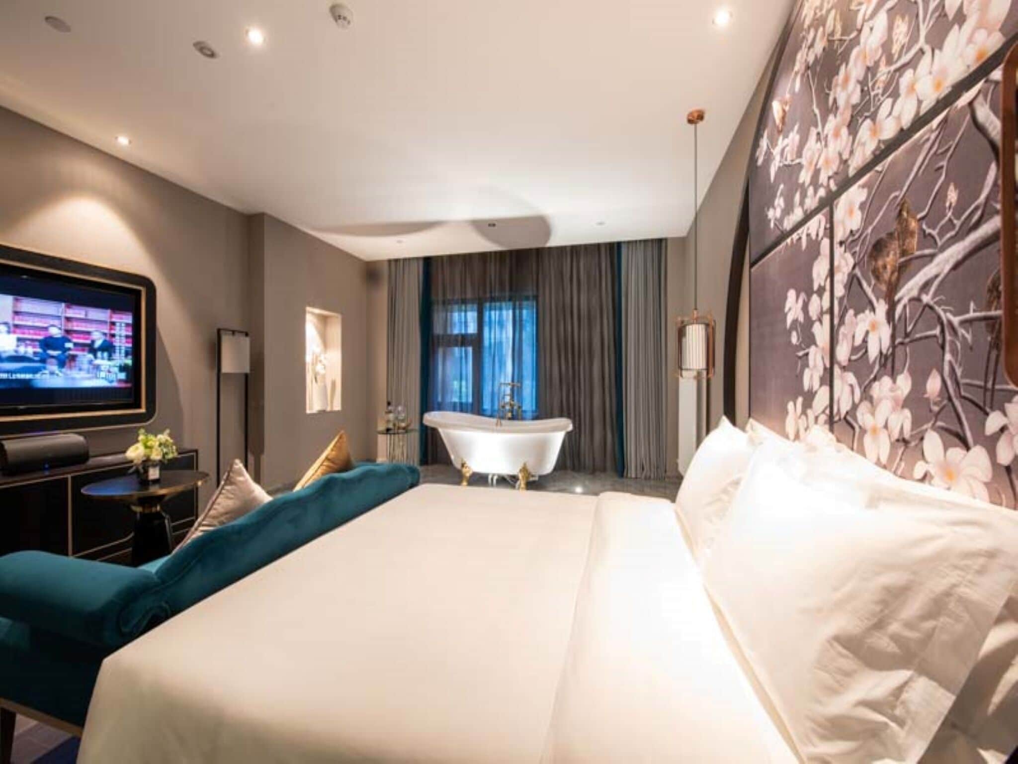 Una habitación de hotel con una cama grande, una bañera, un televisor y una pared con un diseño floral.