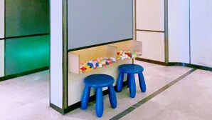 Una habitación con un separador, dos taburetes azules y un estante con objetos de colores.