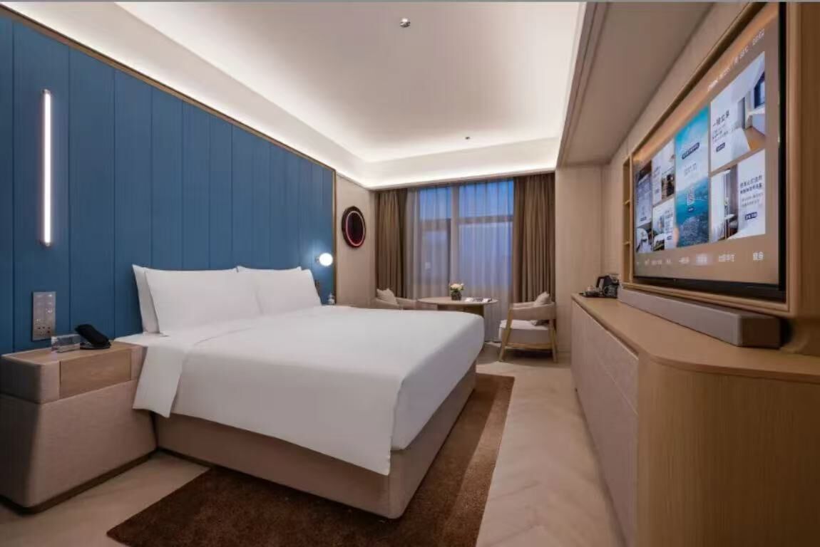 A hotel room with a bed, bedside tables, a TV, and a window with curtains.