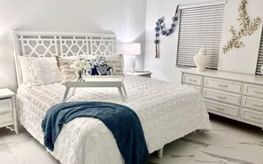 A bedroom with a white bed, a bedside table, a lamp, and a dresser. - Beachfront Island Escape- Heated Pool (Fort Pierce)