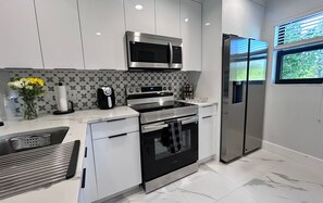 A modern kitchen with stainless steel appliances, a patterned backsplash, and a window with a view. - Beachfront Island Escape- Heated Pool (Fort Pierce)