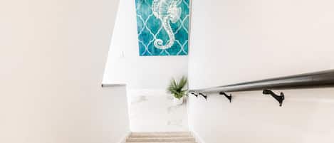 Een trap met een leuning, een potplant en een aan de muur hangend kunstwerk van een zeepaard.
