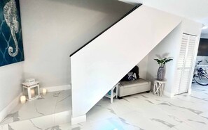 A modern interior with a white staircase, a small seating area, and a wall-mounted artwork. - Beachfront Island Escape- Heated Pool (Fort Pierce)