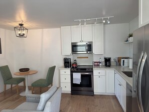 Cozinha moderna com armários brancos, micro-ondas de aço inoxidável e forno embutido. Há uma área de jantar com mesa redonda e duas cadeiras.