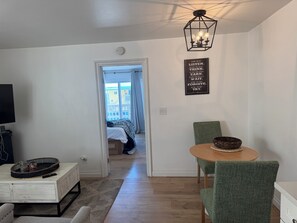 A modern living room with a flat-screen TV, a coffee table with a woven tray, a green upholstered chair, and a dining table with a woven bowl. - ★Imperial Beach Suite Life★ Oceanfront 2BR Dual Suites Steps to Sand (Imperial Beach)