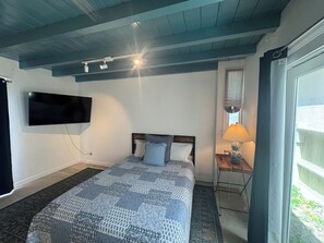 A bedroom with a bed, a TV mounted on the wall, a lamp on a bedside table, and a window with curtains. - ★Imperial Beach Suite Life★ Oceanfront 2BR Dual Suites Steps to Sand (Imperial Beach)