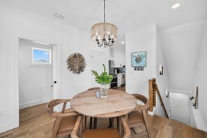 Ein Essbereich mit einem runden Holztisch, Stühlen, einer hängenden Lampe und Blick in die Küche im Hintergrund.