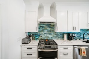 Eine Küche mit weißen Schränken, einem Gasherd, einem Backofen, einer Kaffeemaschine und einer blauen Küchenrückwand.