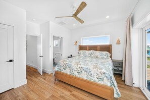 Ein Schlafzimmer mit einem hölzernen Bett, einem Deckenventilator, einem Fenster mit Blick und einer Tür zu einem anderen Raum.