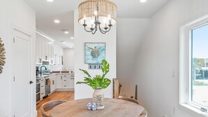 A dining area with a round wooden table, chairs, a hanging light fixture, and a view of the kitchen in the background. - Double D's by the Sea | New 2BR Coastal Retreat (Mexico Beach)