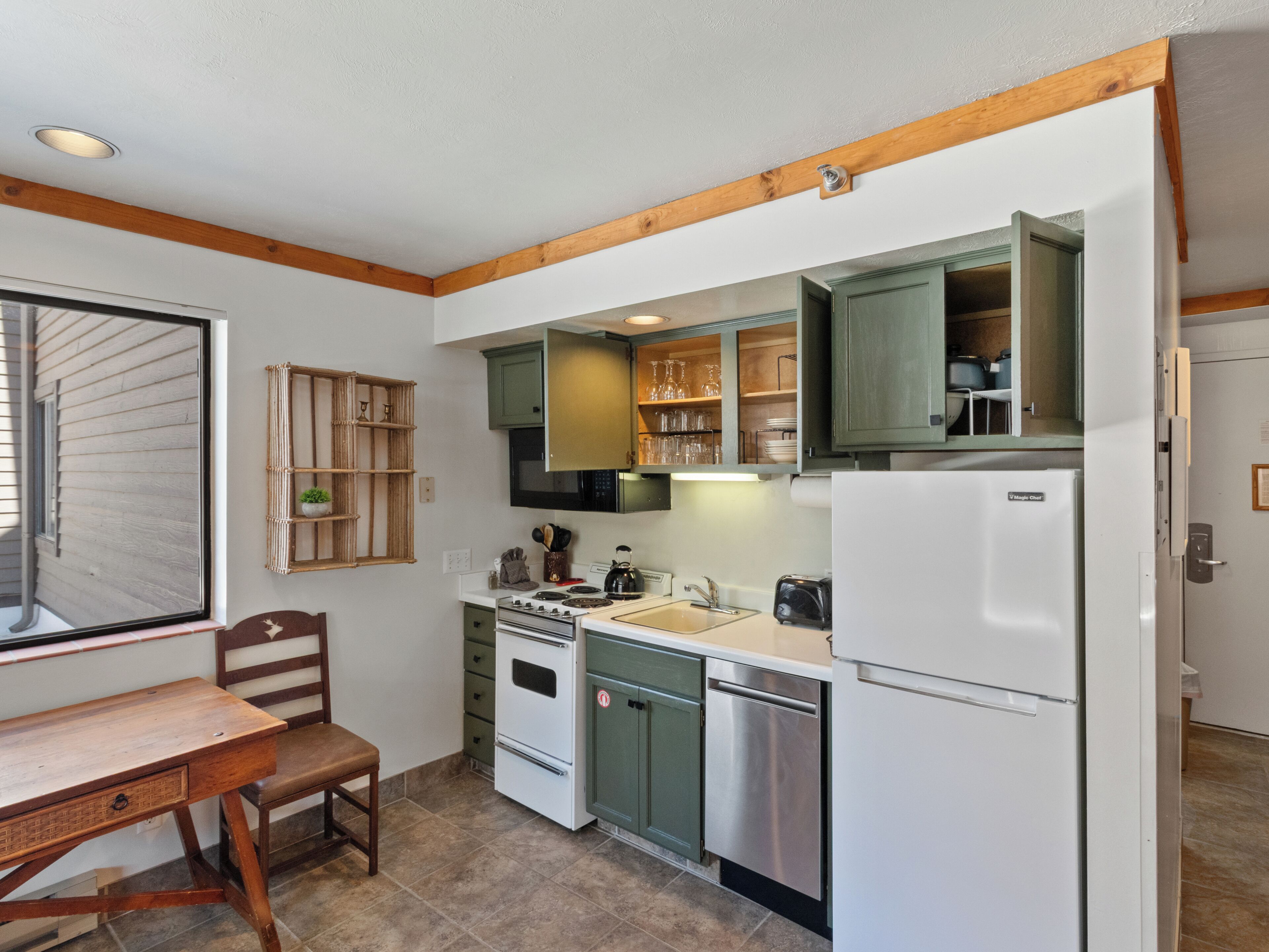 A kitchen with a wooden ceiling, a stove, a sink, and green cabinets.