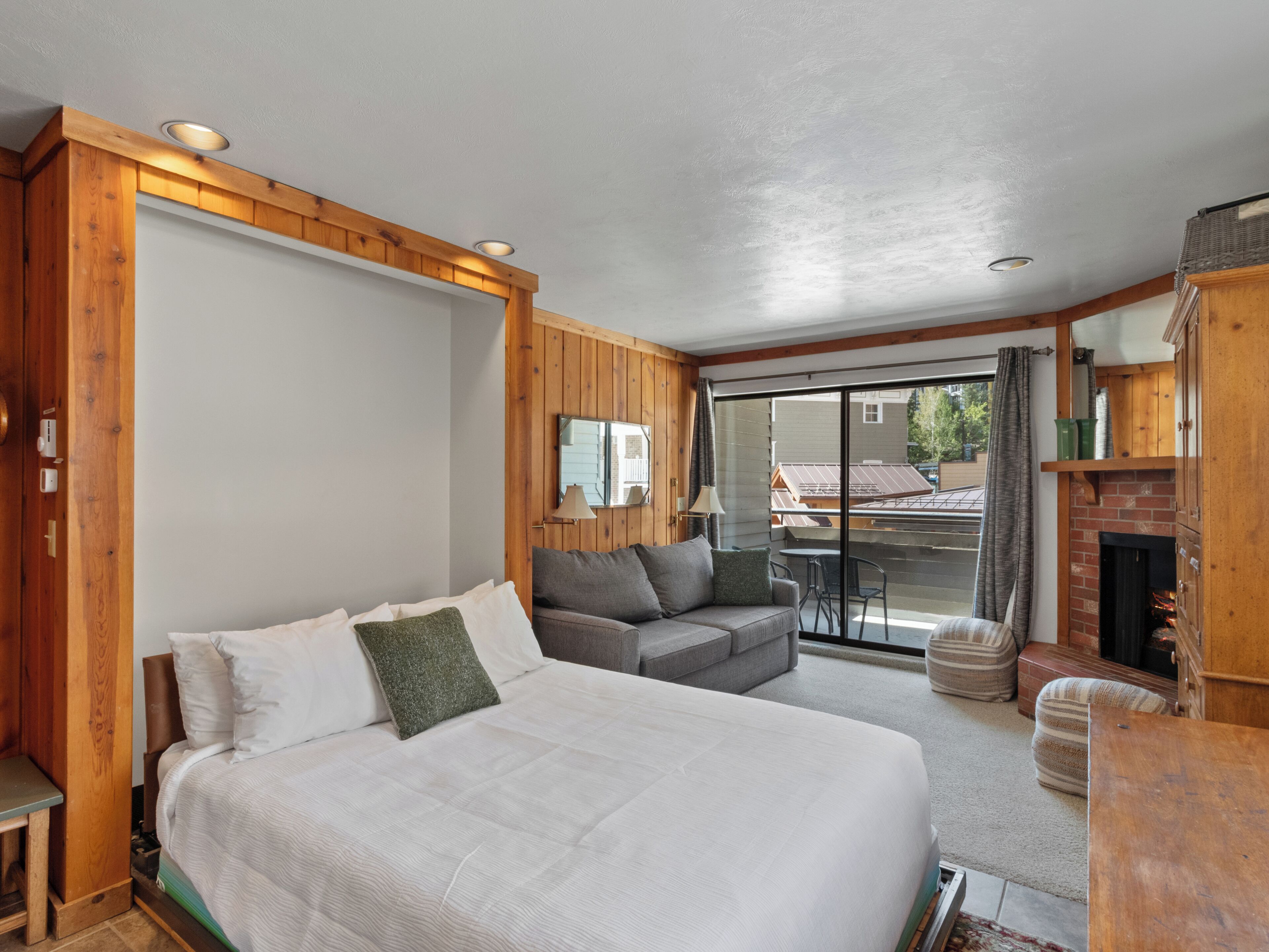 A bedroom with a bed, a sofa, a fireplace, and a view of the outside.