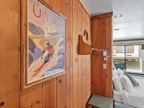 A room with wooden walls, a framed poster of a skier, a wooden guitar, and a bed with pillows. - Lodge at Mtn Village A223 | Ski-In/Out | PCMR Views | Pool & Hot Tubs (Park City)