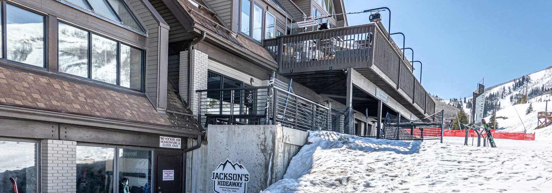 A building with a ski lift, a sign for 'Jackson's Hideaway Park City Utah,' and a snow-covered slope.
