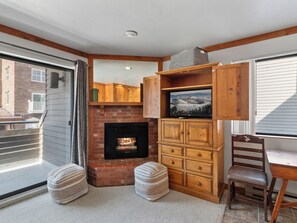 Een gezellige woonkamer met een open haard, houten kasten, een televisie en een comfortabele zithoek.