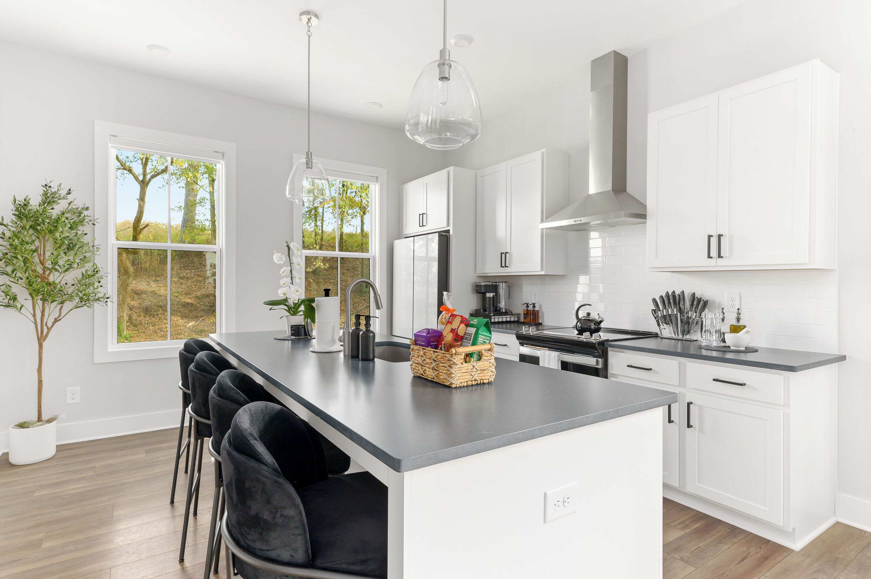 A modern kitchen with white cabinetry, a central island, bar stools, and a view of the outdoors.