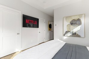 Une chambre d’hôtel avec un lit, un téléviseur fixé au mur qui affiche « NETFLIX », et un tableau abstrait encadré.