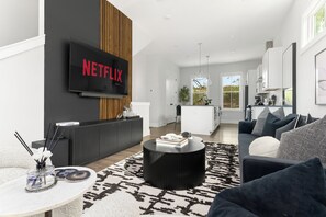 Un salon moderne avec un téléviseur à écran plat affichant le logo « NETFLIX », un canapé noir, une table basse et un tapis à motifs.