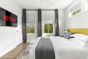 Une chambre à coucher moderne avec un grand lit, un téléviseur fixé au mur et une fenêtre avec des rideaux.