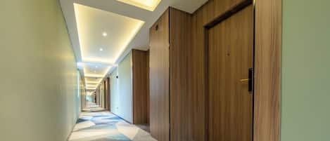Un pasillo de hotel con puertas de madera, alfombra estampada e iluminación empotrada en el techo.