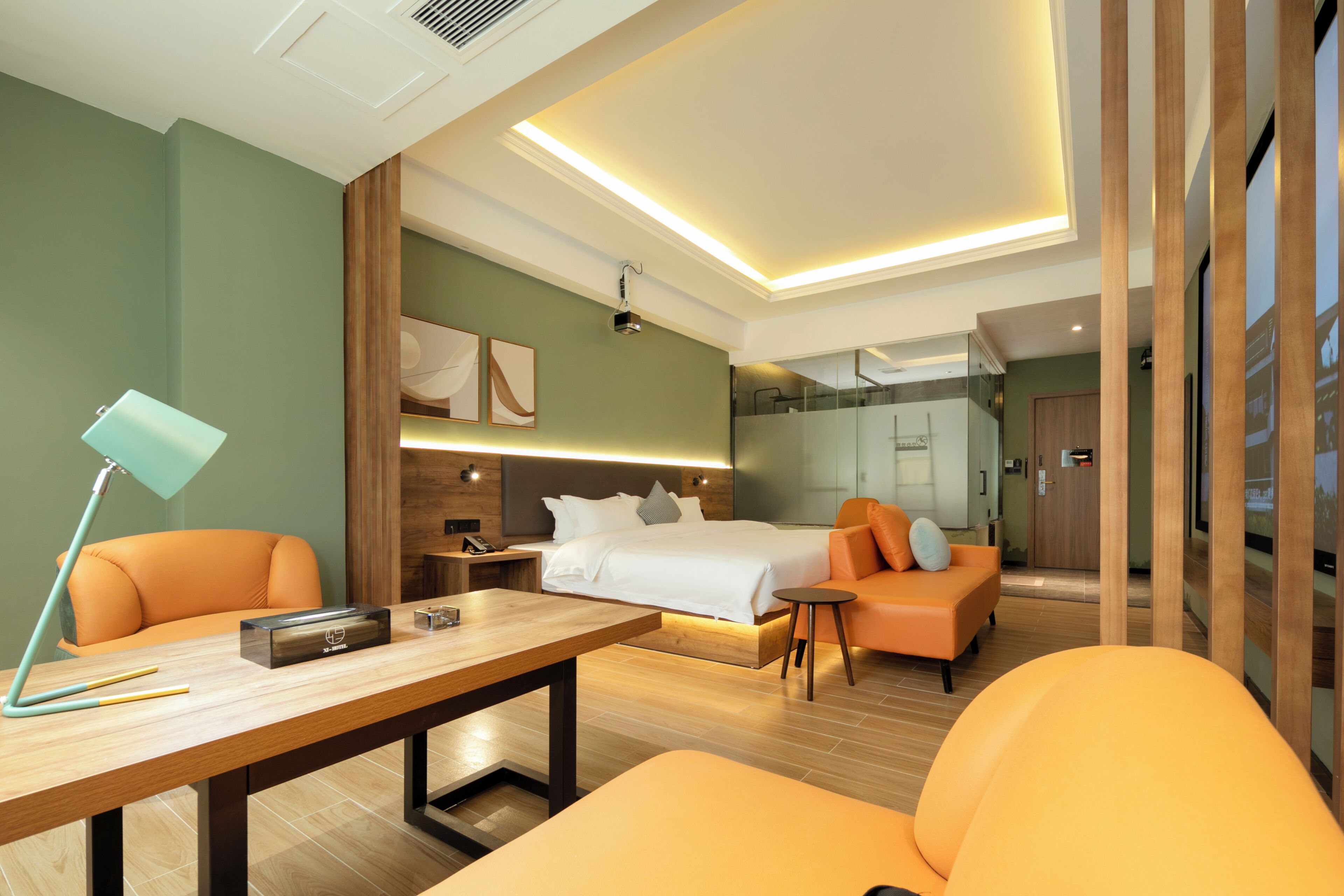 Ein Hotelzimmer mit Bett, Schreibtisch, Stuhl, Sofa und einem durch eine Glaswand abgetrennten Badezimmer.