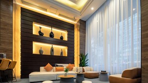 Um lobby moderno com um sofá, pufes e uma mesa de centro. Há vasos decorativos em prateleiras e uma planta.