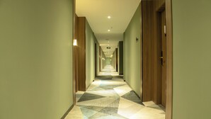 Corredor de hotel com carpete estampado, portas de madeira e teto com iluminação embutida.